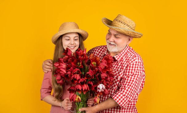 happy old grandfather with granddaughter hold tulip flowers on yellow background. womens day - Foto, immagini