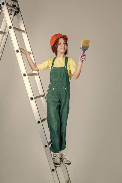 can fix anything. kid builder on construction site. worker engineer. architect in workshop. renovation and repair. teen girl in helmet and boilersuit on stepladder. child on ladder wear hard hat - Foto, Bild