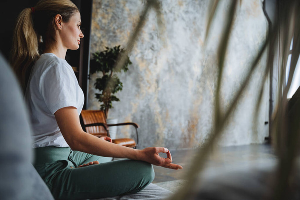 A beautiful girl in a tracksuit meditates, folding fingers into mudras. Assanas for reassurance. Relaxation by yoga and sports.Harmony with yourself. High quality photo - Fotografie, Obrázek