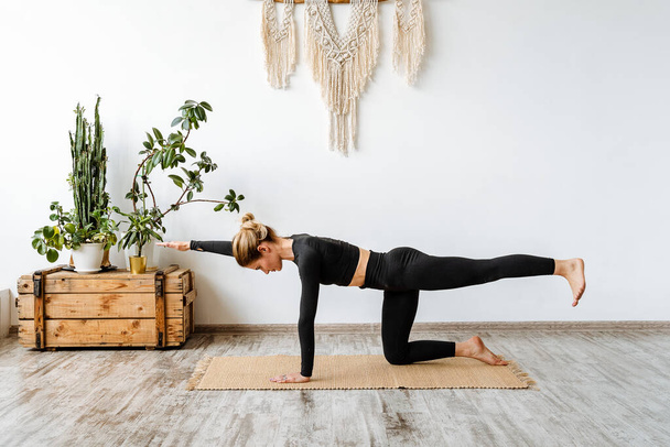 Bidalasana cat pose. A young girl practicing yoga while standing on one knee pulls her hand forward. Gymnastics for muscles, morning warm-up in a cozy house. High quality photo - Foto, afbeelding