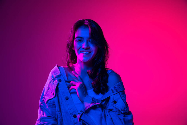Beautiful young emotional girl, student with long dark hair isolated on gradient pink-blue background in neon light. Concept of emotions, youth - Fotografie, Obrázek