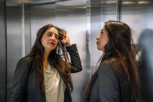 Добре одягнена іспанська бізнесменка, яка торкається волосся у ліфті. - Фото, зображення