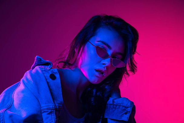 Youth culture. Beautiful young emotional girl, student with long dark hair isolated on gradient pink-blue background in neon light. - Φωτογραφία, εικόνα