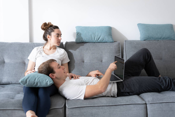 Nuori pari surffaa verkossa kannettavan tietokoneen rentoutuessa sohvalla - Valokuva, kuva