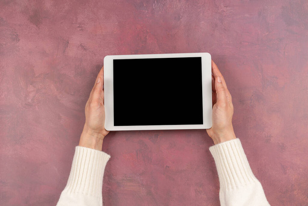 Woman hand holding digital tablet computer with blank screen mock up on pink color background. Top view, copy space - 写真・画像