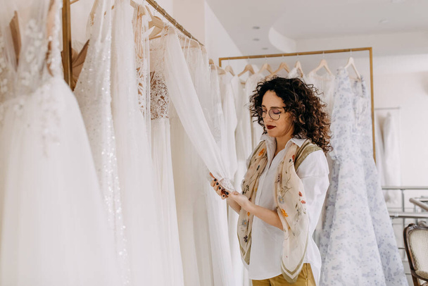 Frau wählt Brautkleid in einem Showroom. Zukünftige Braut kauft Hochzeitskleid im Geschäft. - Foto, Bild