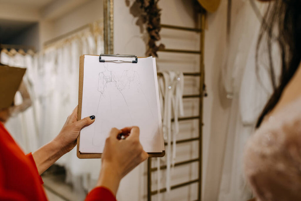 Stilista di moda che mostra schizzi di abiti da sposa a un cliente in uno showroom. - Foto, immagini