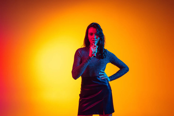 Beautiful young excited girl, student with long dark hair isolated on gradient yellow background in neon light. Concept of emotions, youth - Fotó, kép