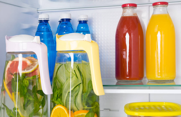 against the background of a white refrigerator, on the shelves are soft drinks, citrus lemonade in a jug, bottled water and juices - Foto, immagini