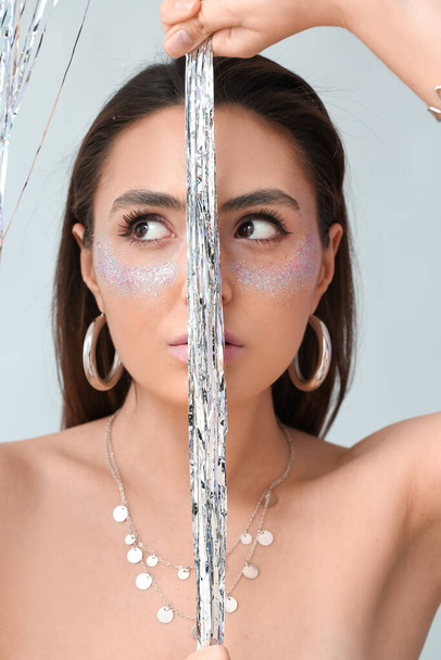 Beautiful young woman with glitters on her face against light background - Fotó, kép