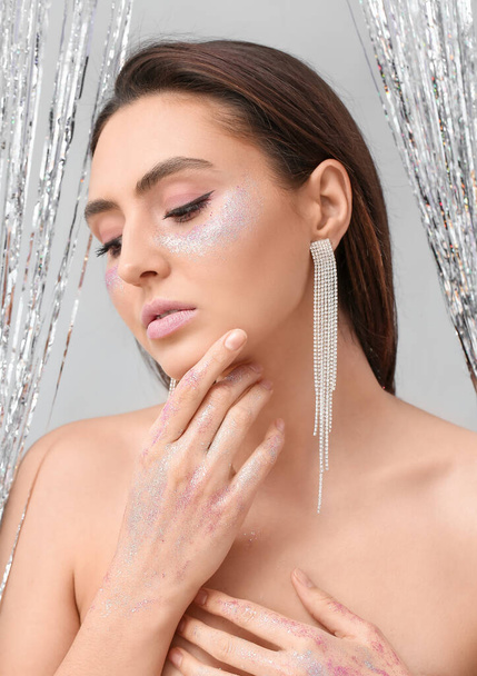 Beautiful young woman with glitters on her face against light background - Fotoğraf, Görsel