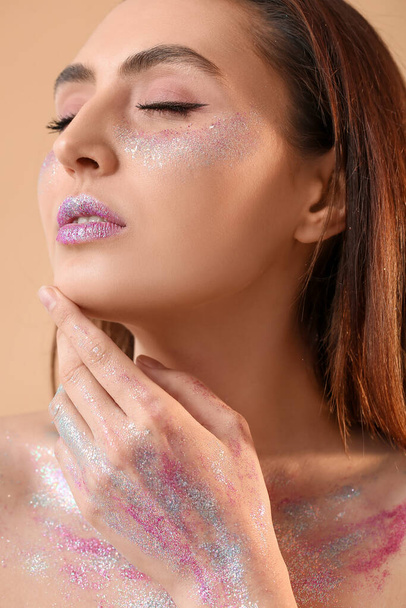 Beautiful young woman with glitters on her face and body against color background - Photo, Image