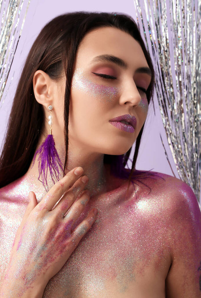 Beautiful young woman with glitters on her face and body against color background - Foto, afbeelding