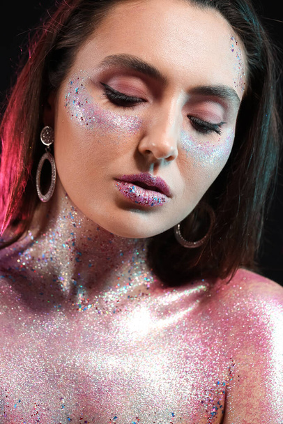Beautiful young woman with glitters on her face and body against dark background - Φωτογραφία, εικόνα