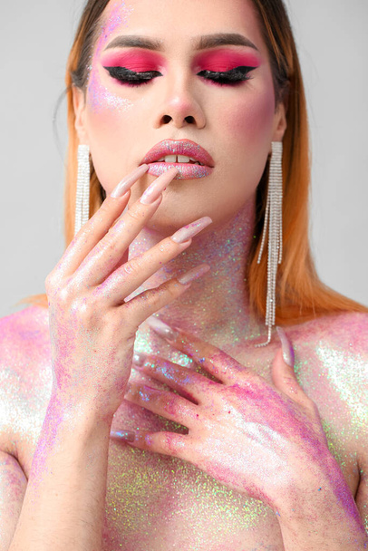 Mujer transgénero joven de moda con purpurina en el cuerpo contra el fondo claro - Foto, imagen