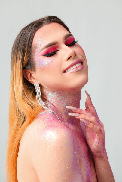 Modna młoda transseksualistka z brokatami na ciele na jasnym tle - Zdjęcie, obraz