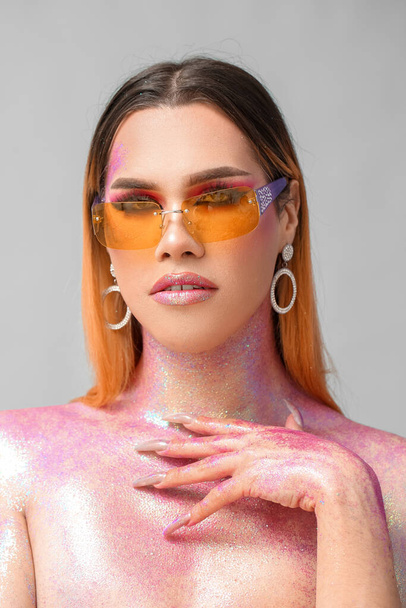 Модная молодая трансгендерная женщина с блестками на теле на светлом фоне - Фото, изображение
