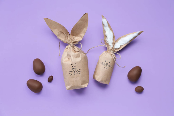 Великодній кролик подарункові пакети та шоколадні яйця на бузковому фоні
 - Фото, зображення