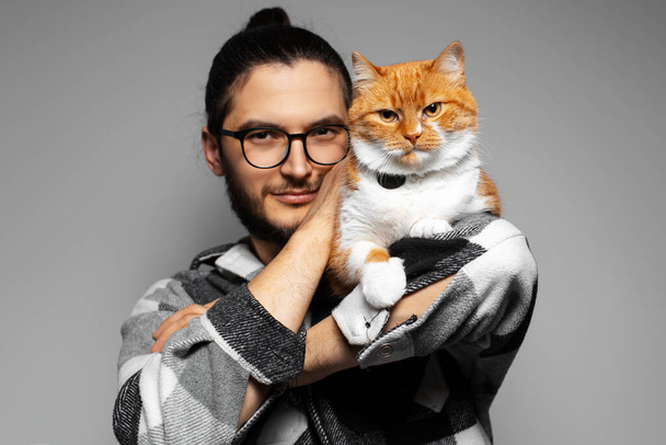 Studio portrait of young man with red cat on his shoulder. Grey background. - Photo, Image