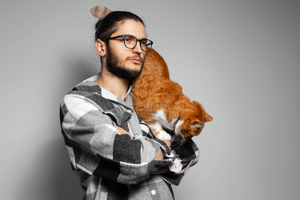 Studio portrait of young man with red cat on grey background. - Photo, Image