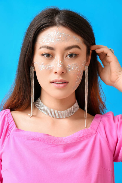 Portrait of Asian woman with glitter makeup and stylish jewelry on color background - Photo, Image