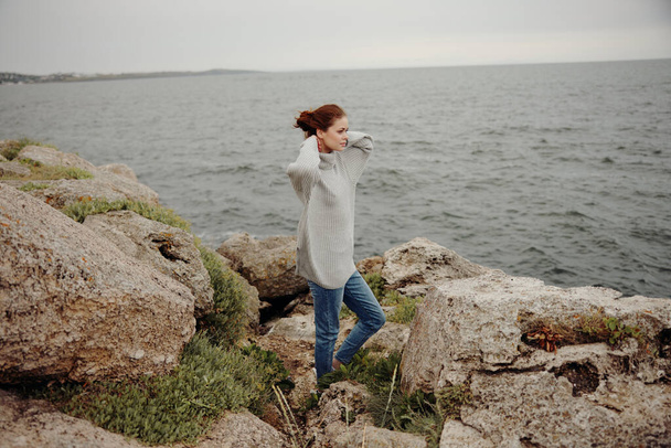 beautiful woman in a gray sweater stands on a rocky shore nature female relaxing - Foto, imagen