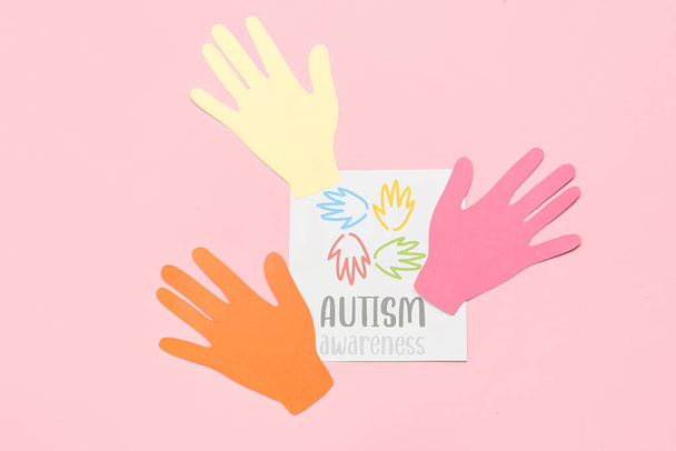 Paper sheet with text AUTISM AWARENESS and paper human palms on pink background - Photo, Image