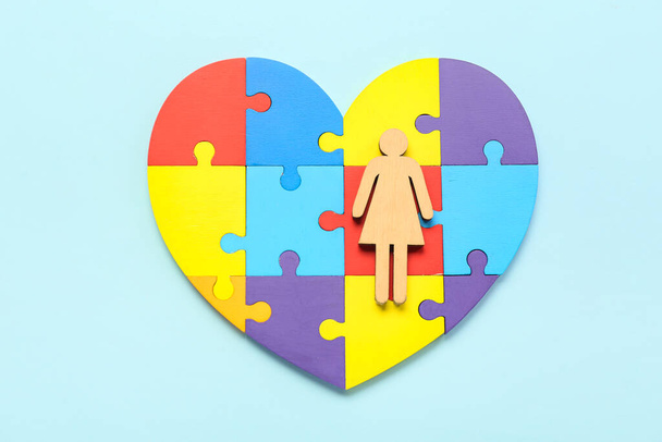 Hart gemaakt van puzzelstukjes en houten vrouwelijke figuur op blauwe achtergrond - Foto, afbeelding