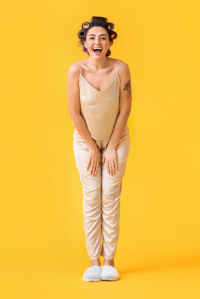 Boldog fiatal nő a haj görgők sárga háttér - Fotó, kép