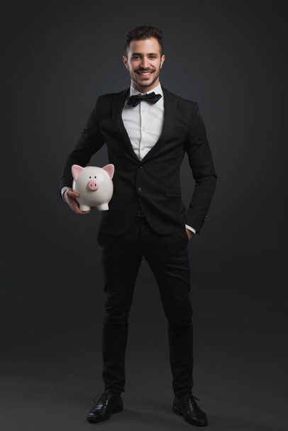 Man in tuxedo holding a pig money box - Zdjęcie, obraz