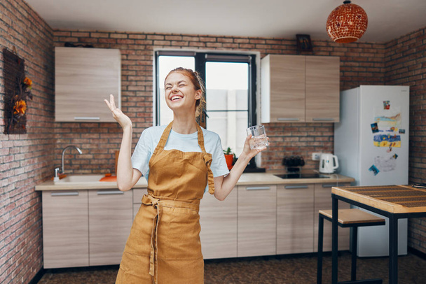 mulher em um copo avental marrom de água cozinha interior Estilo de vida - Foto, Imagem