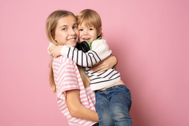 Młodszy brat i siostra razem w luźnych ubraniach stojących na różowym tle. Koncepcja stylu życia. - Zdjęcie, obraz