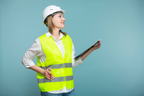 Professioneel ingenieur. Een vrouw met een helm en heldere gelei gebruikt een tablet, op een blauwe achtergrond. Kopieerpasta. - Foto, afbeelding