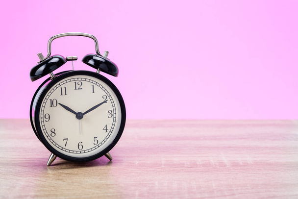 Reloj despertador retro negro sobre mesa de madera con fondo rosa. - Foto, imagen