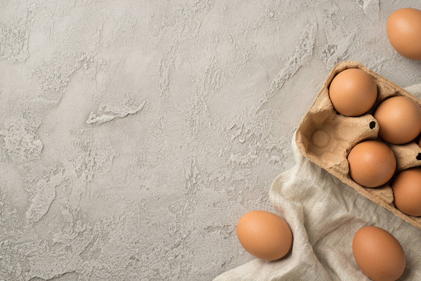 Horní pohled fotografie velikonoční dekorace hnědé velikonoční vejce ručník a držák na vejce na izolovaném šedém betonu pozadí s prázdným prostorem - Fotografie, Obrázek