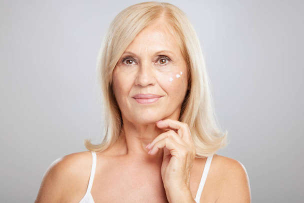 An attractive blond senior woman putting anti-age creme. Beauty photography - Fotó, kép