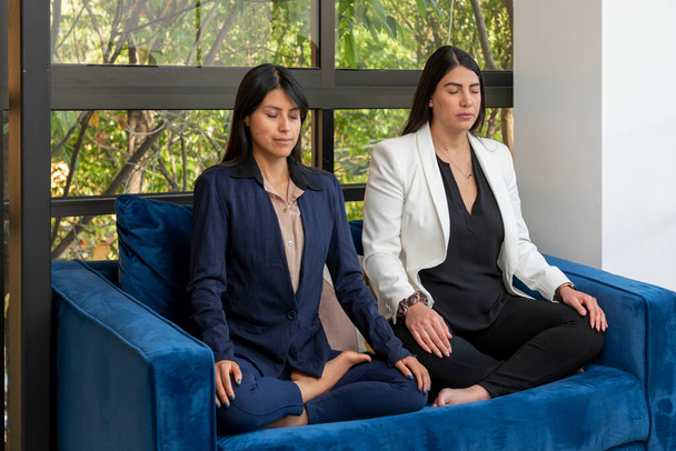 Oldalnézet két üzletasszony meditál egy karosszéken, miközben szünetet tartanak az irodában.. - Fotó, kép