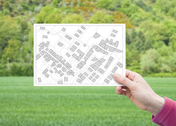 Telkek kezelése - ingatlan koncepció egy üres földterülettel egy zöld lakóterületen elérhető építési kézzel kezében egy képeslapot egy képzeletbeli kataszteri térkép - Fotó, kép