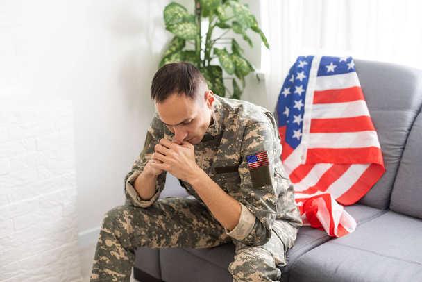 Sad soldier in uniform covering his mouth while sitting on a sofa - 写真・画像