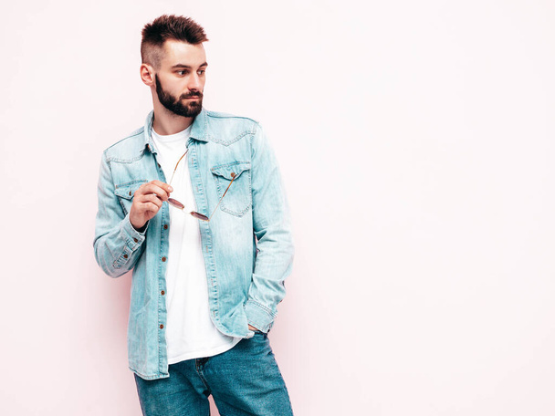 Portrait of handsome confident stylish hipster lambersexual model.Man dressed in jacket and jeans. Fashion male posing in studio in sunglasses. Isolated on light pink - Φωτογραφία, εικόνα