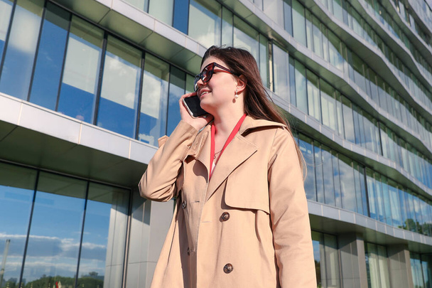 Młoda kobieta w ubraniu biznesowym rozmawia przez telefon w tle budynku biurowego - Zdjęcie, obraz