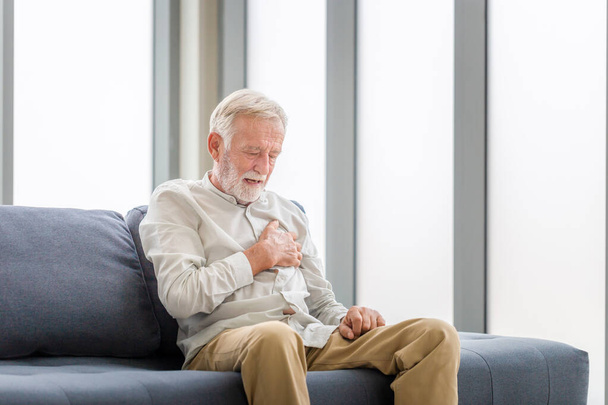 Senior man drukt hand in borst heeft een hartaanval lijdt aan ondraaglijke pijn, Man met pijn op het hart in de woonkamer - Foto, afbeelding