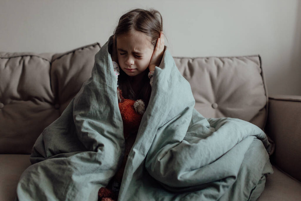 Stop de oorlog. Bid voor Oekraïne. Wij staan aan de kant van Oekraïne. Oekraïense bange kind onder een deken. Het meisje is bang voor de geluiden van luchtaanvallen en explosies. Arm kind met verdriet en verdriet, pech en verdriet.  - Foto, afbeelding