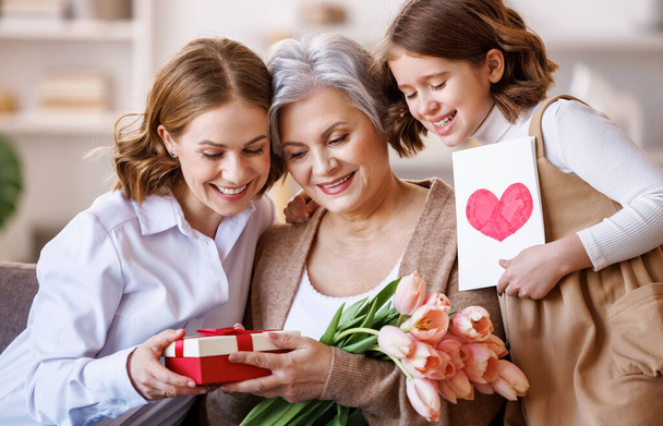 З Міжнародним днем жінок. Дочка з внучкою дарують бабусі квіти і святкують День матері вдома. - Фото, зображення