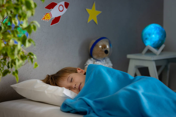 Happy child sleeping with toy rocket and teddy bear. Kid pretend to be astronaut. Imagination and children dream concept - Фото, зображення