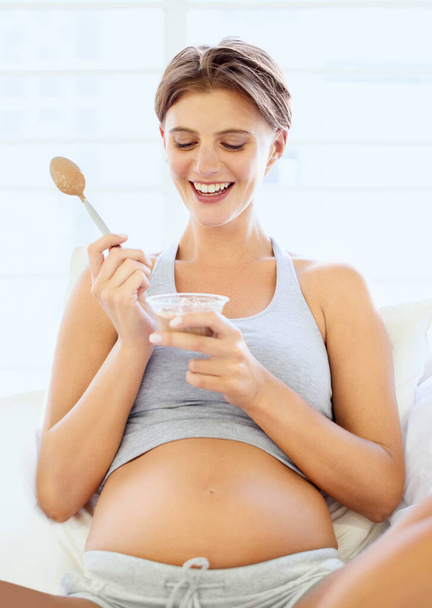 Mommy needs some sugar. A happy young pregnant woman eating a small bowl of pudding. - Foto, Imagem