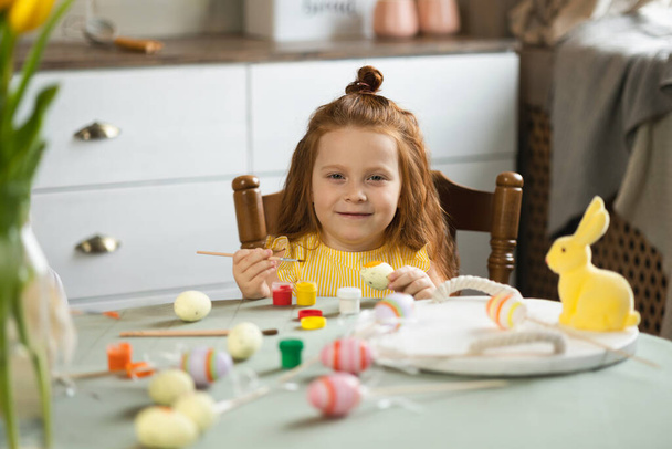 Portrait of cute little girl with brush coloring Easter eggs - Valokuva, kuva