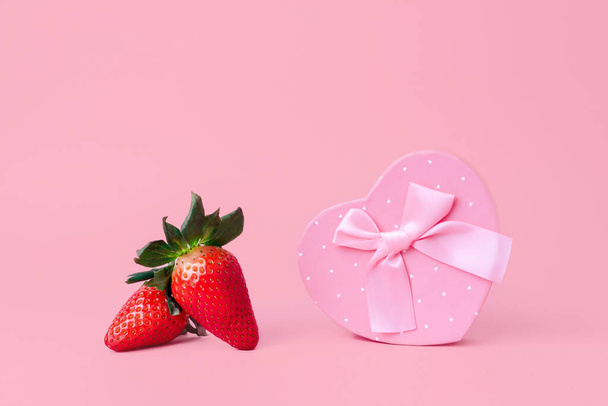 Delicious red strawberries next to a heart with a ribbon. Pastel pink background - Zdjęcie, obraz