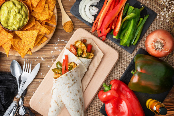 Chicken fajitas with peppers, onion and spices and guacamole sauce with tortilla chips or nachos on a wooden table - Photo, Image