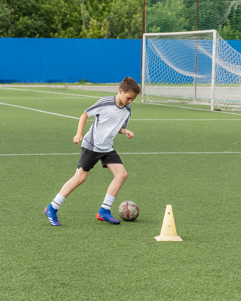 Ulyanovsk|Russia-July 16, 2021: The boy loves to play football, trains with the ball on the artificial turf and scores a goal. The boy plays football. - Foto, afbeelding
